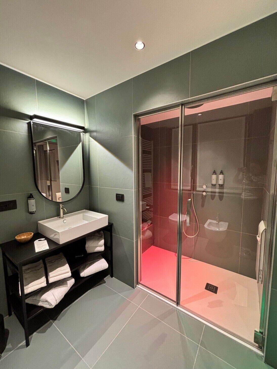 Un bagno moderno con uno specchio grande, un lavandino, un mobile bagno nero e un'area doccia vetrata.