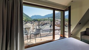 A bedroom with a large window overlooking a balcony with a view of mountains and a church. - Hotel Stelvio Tirano (Tirano)
