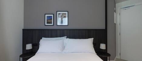 A hotel room with a large bed, two bedside tables with lamps, a dark headboard, and two framed pictures on the wall.