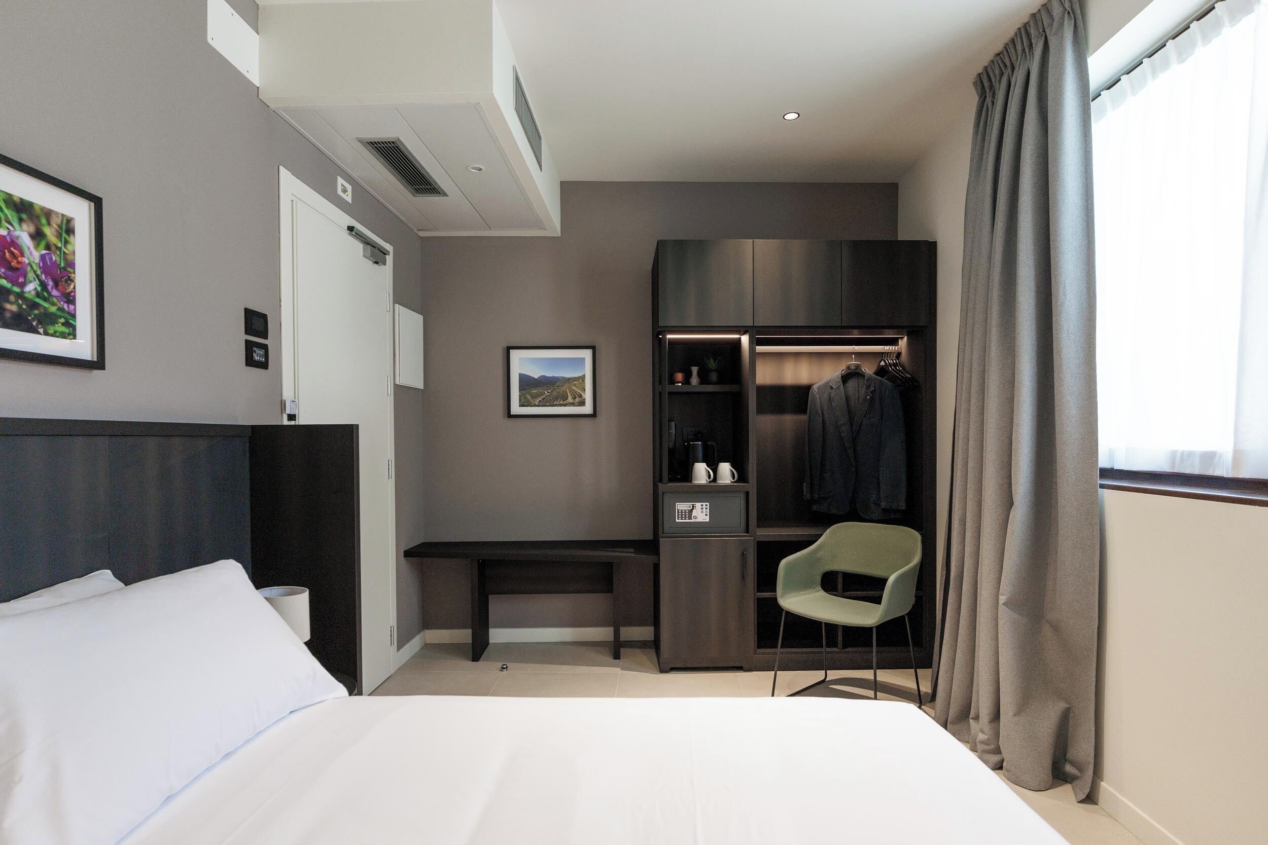 Een hotelkamer met een bed, bureau, stoel, kast en raam met gordijnen.