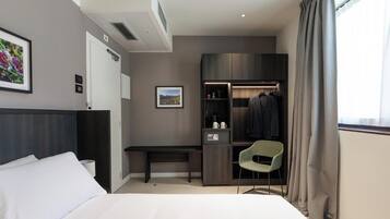 Een hotelkamer met een bed, bureau, stoel, kast en raam met gordijnen.