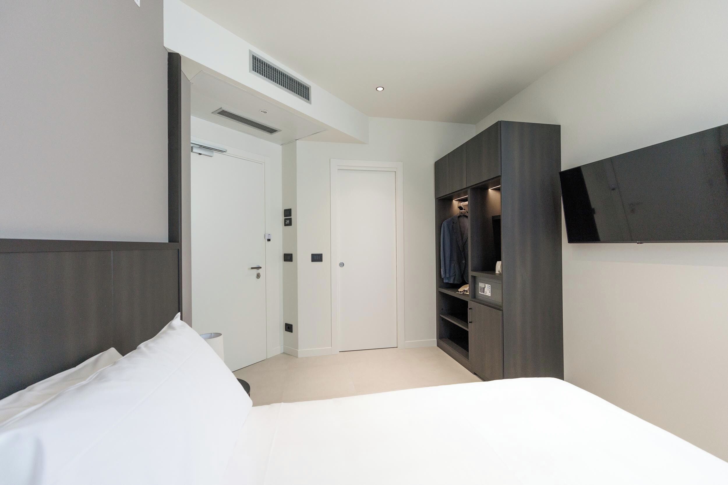 A modern bedroom with a bed, a wardrobe, and a TV mounted on the wall.