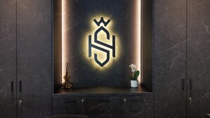 A dark wooden cabinet with a lit-up emblem on the back wall, a small potted plant, and a decorative item on the shelf. - Hotel Stelvio Tirano (Tirano)