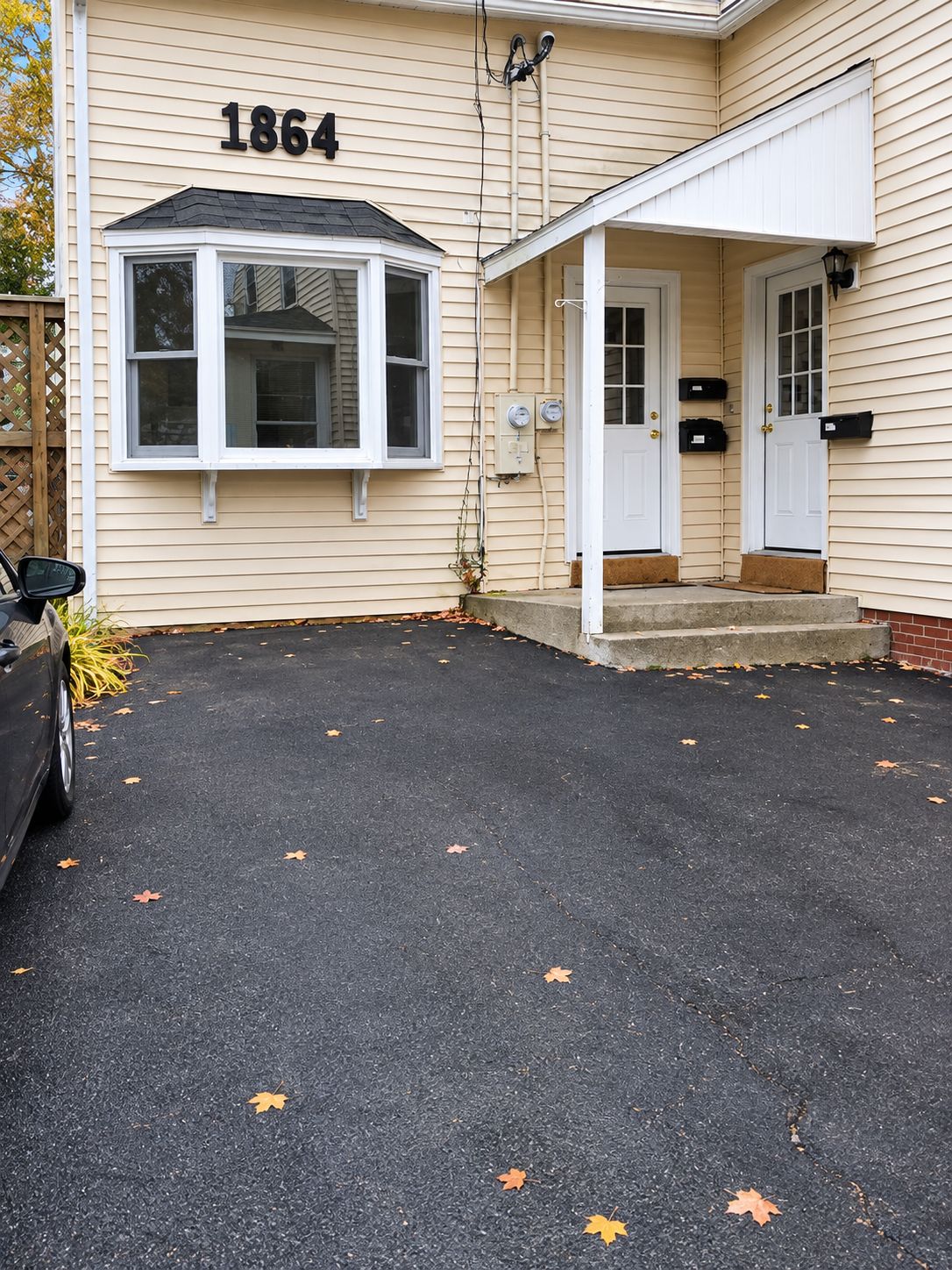 A house with the number 1864 on the side, a covered porch, and a car parked in front.