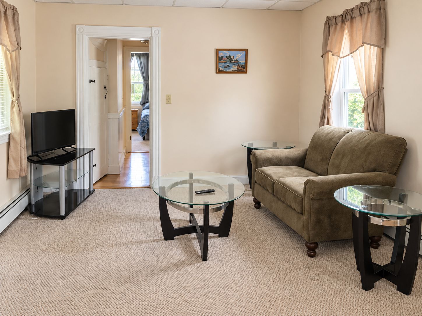 A living room with a sofa, two glass tables, a TV on a stand, and a door leading to another room.