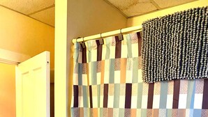 A bathroom with a checkered shower curtain, a white door, and a towel rack with a patterned towel. - Portland 1-bedroom with enclosed porch & parking (Portland)