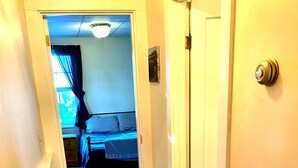 A narrow hallway with wooden flooring leading to a bedroom with a bed and a nightstand. - Portland 1-bedroom with enclosed porch & parking (Portland)