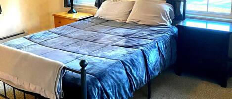A bedroom with a bed, a nightstand, a lamp, and a window with curtains.