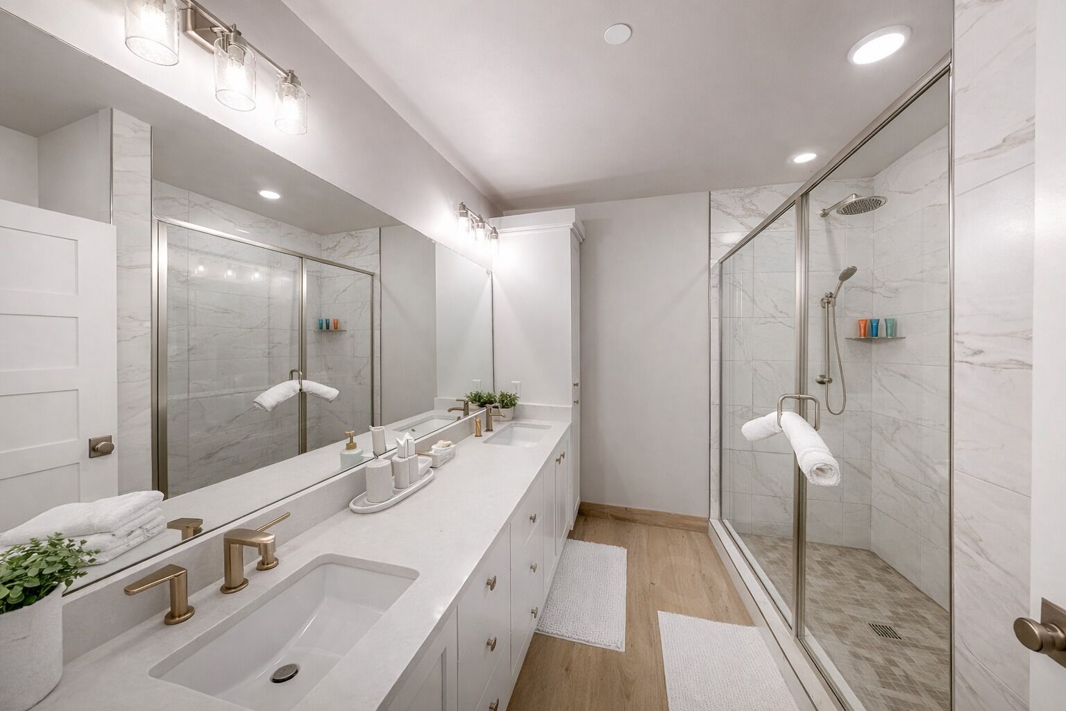 Un baño moderno con un espejo grande, dos lavamanos, una ducha y una planta en maceta.