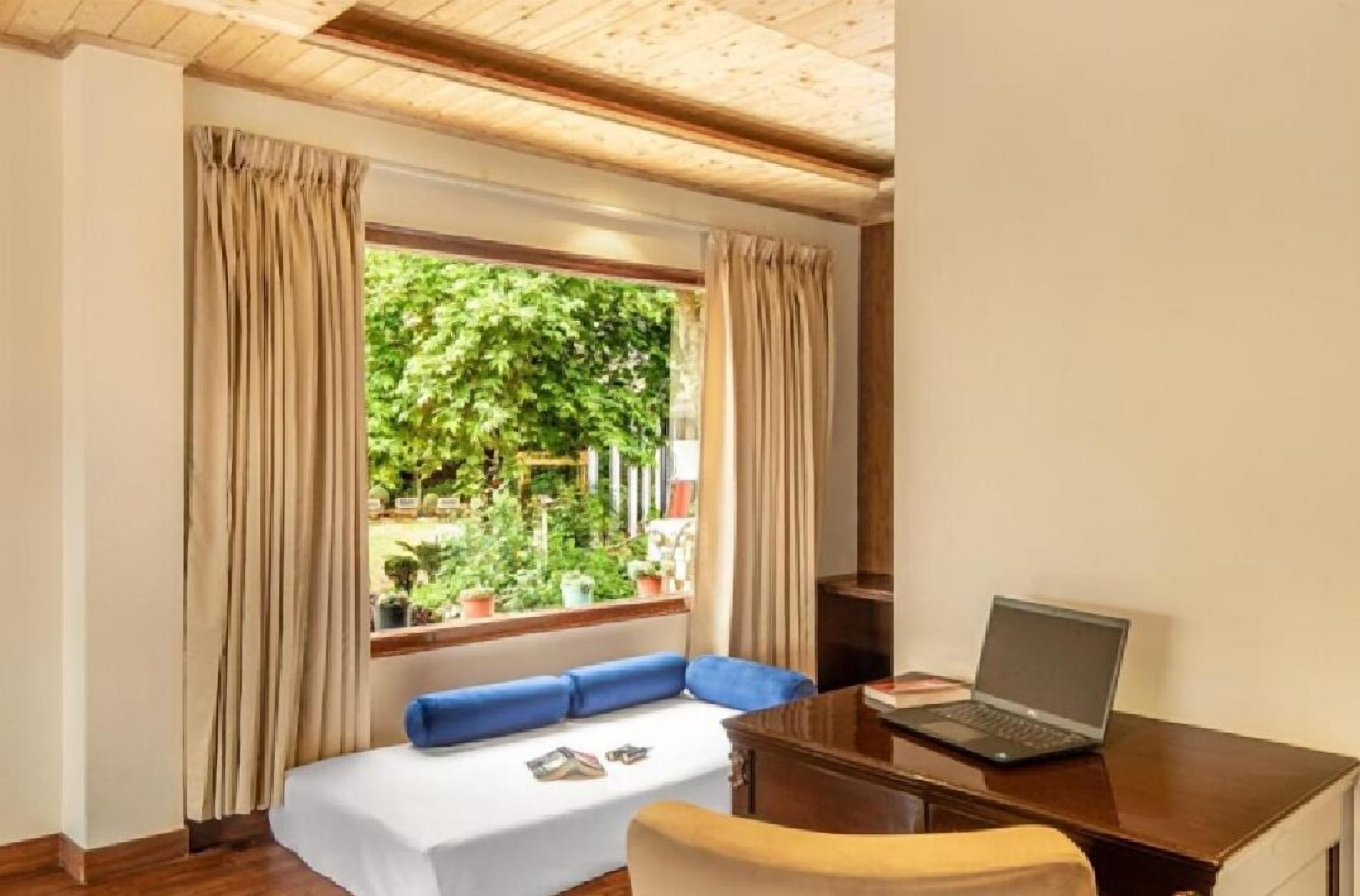 Una habitación con cama, un escritorio con una computadora portátil y una ventana con cortinas.