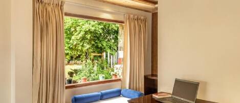 A room with a bed, a desk with a laptop, and a window with curtains.