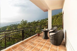 A balcony with a view of a mountainous landscape, a potted plant, and wicker furniture. - Maple Resort Chail (Chail)