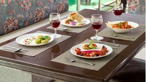 A dining table with a floral sofa, two plates of food, and two glasses of red wine. - Maple Resort Chail (Chail)