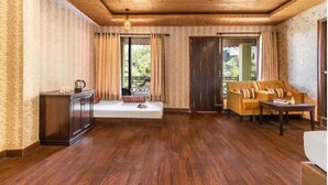 A room with wooden flooring, a sofa, a small table, a cabinet, and a bed. - Maple Resort Chail (Chail)