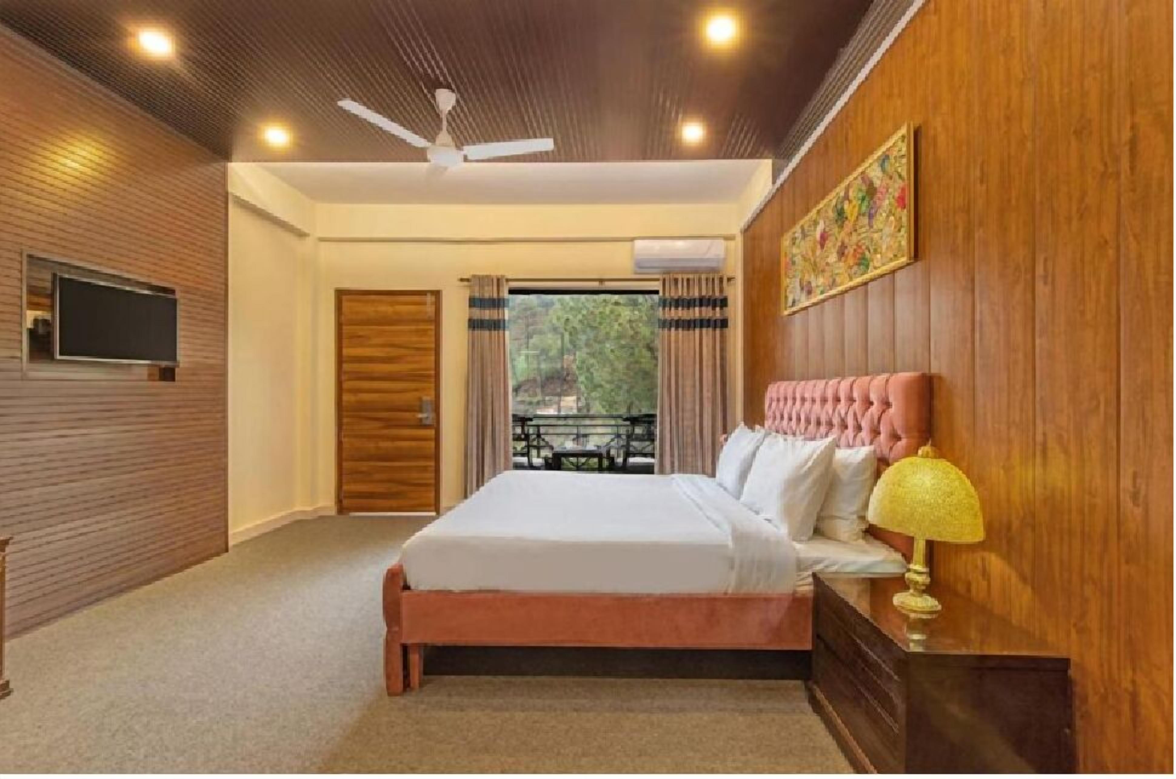A bedroom with a large bed, a ceiling fan, a TV, and a window with curtains.