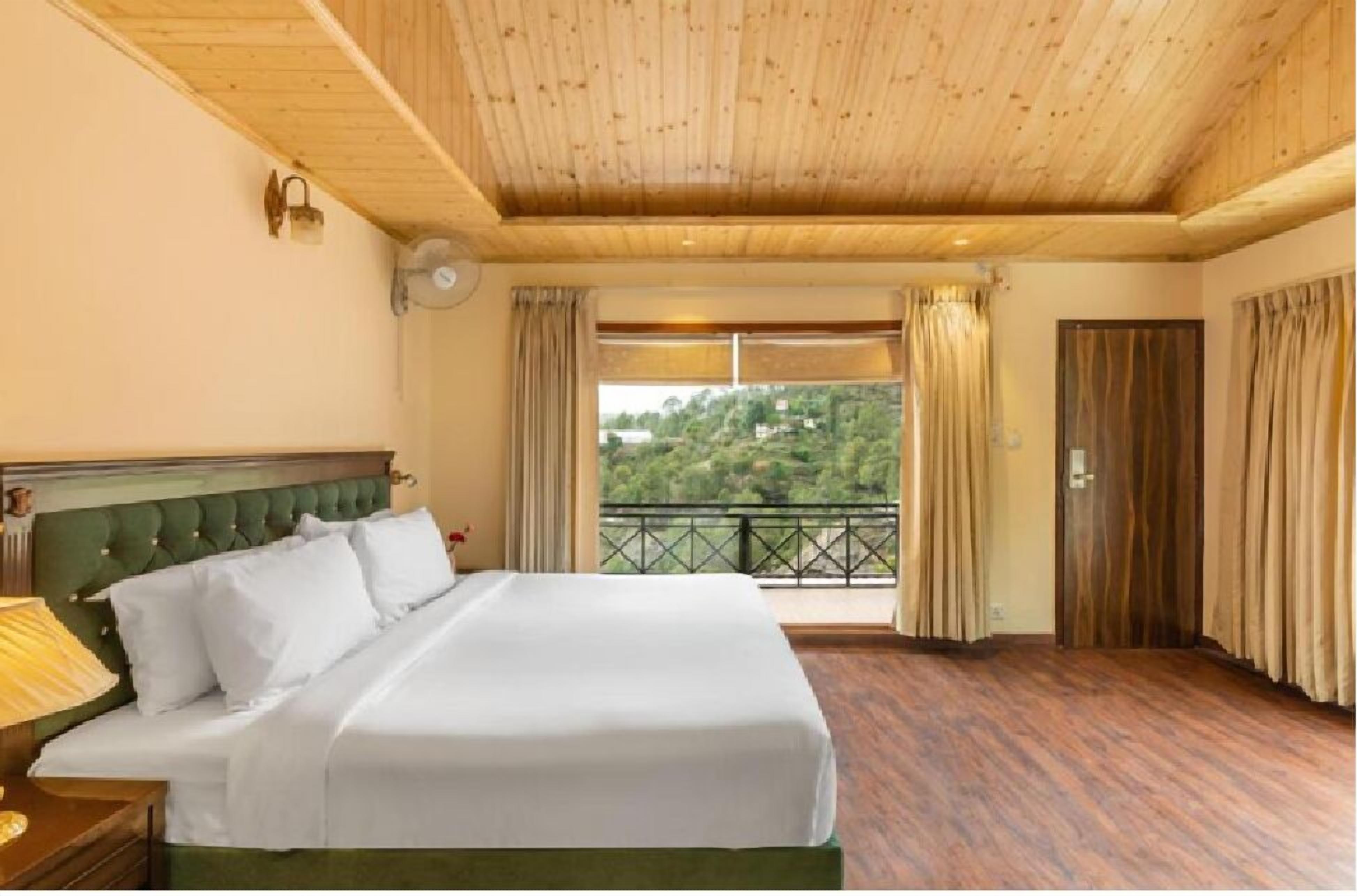 A hotel room with a large bed, wooden ceiling, and a balcony with a view of greenery.