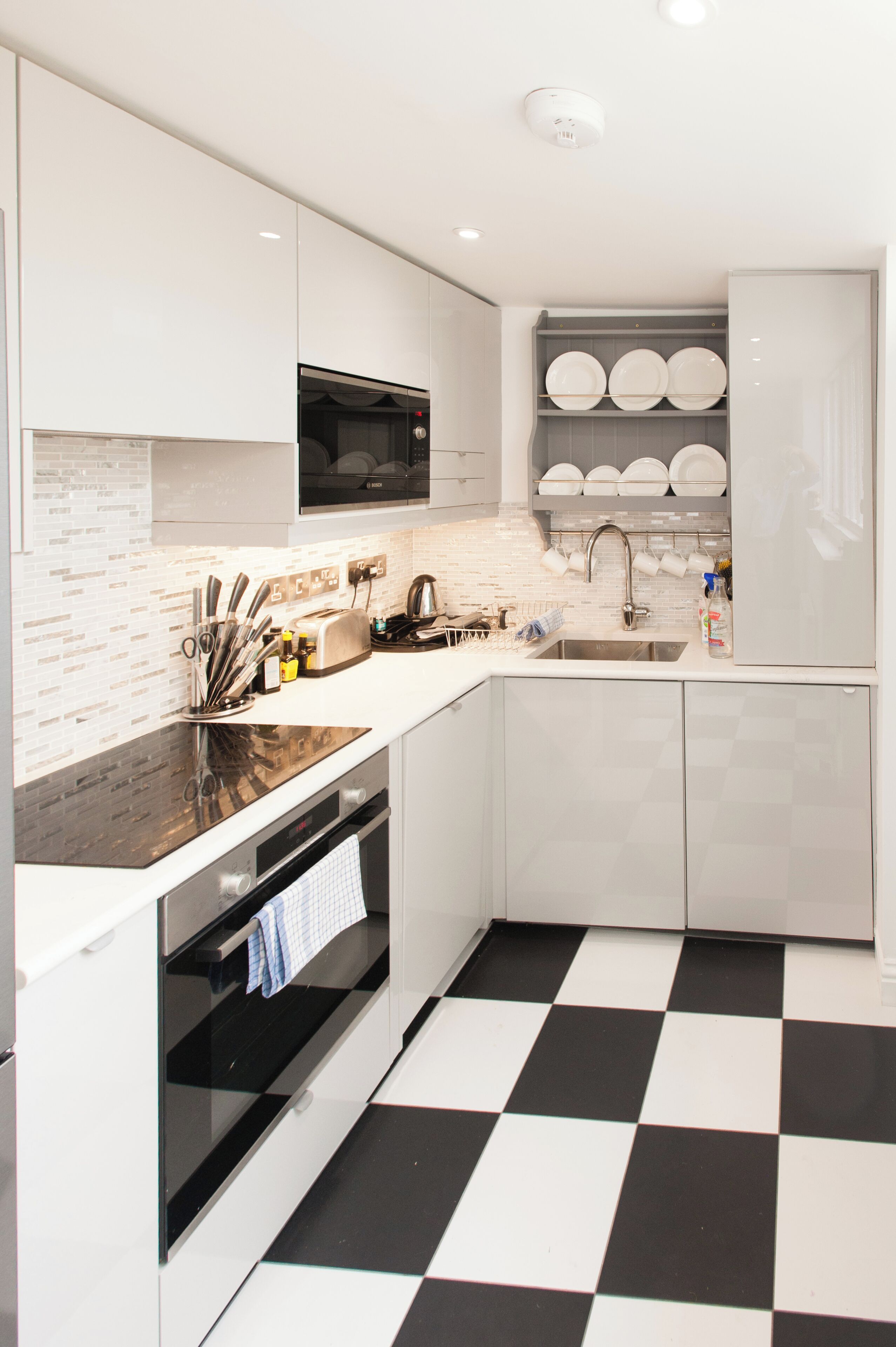 A modern kitchen with white cabinetry, a black and white checkered floor, a microwave, and a dish rack.