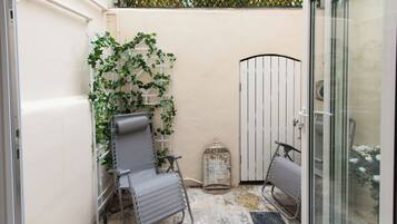 A small, enclosed patio area with two metal chairs, a metal birdcage, and a white gate.