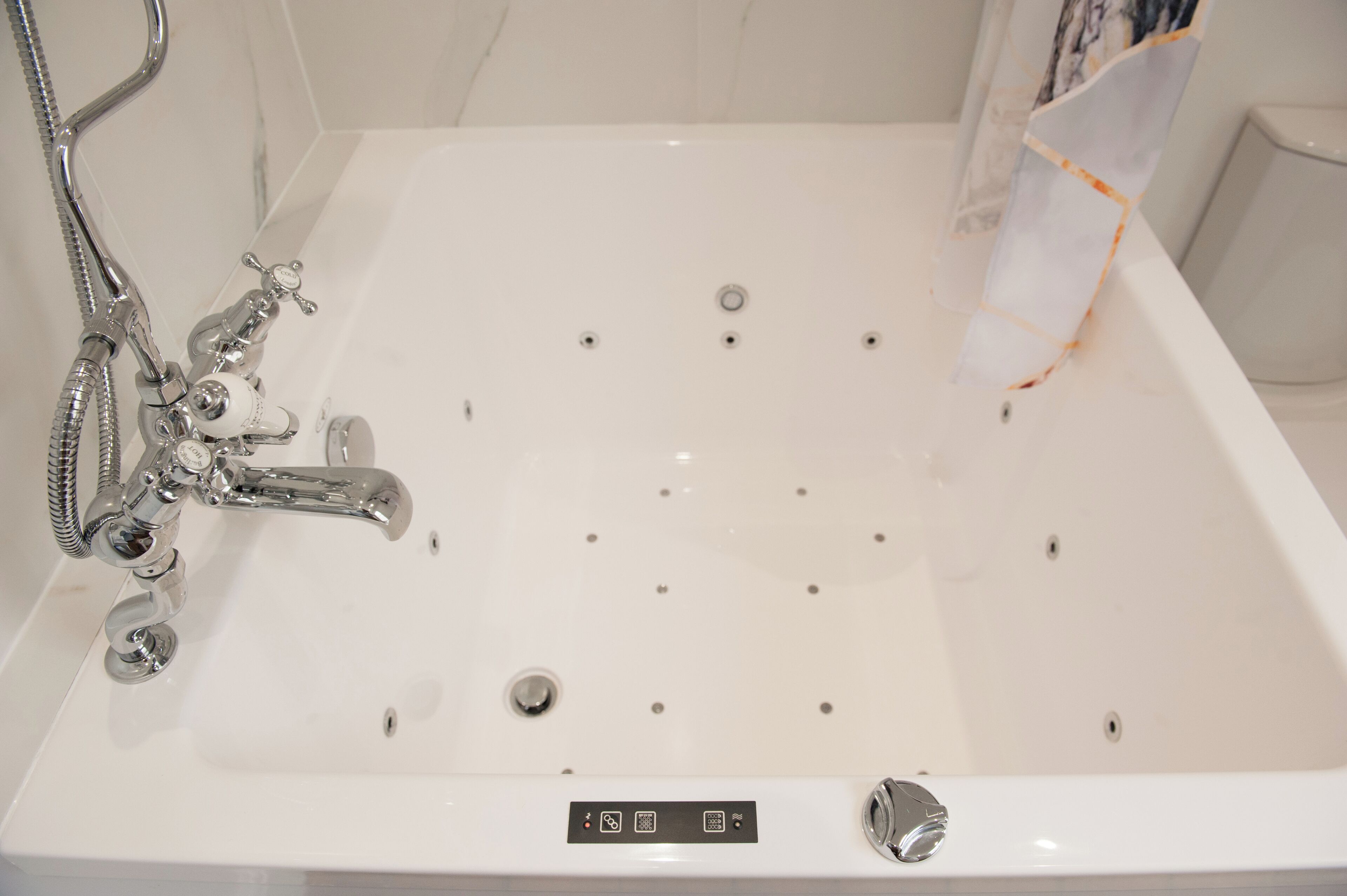 Una bañera blanca con grifo y ducha cromados, un panel de control con iconos y un desagüe.