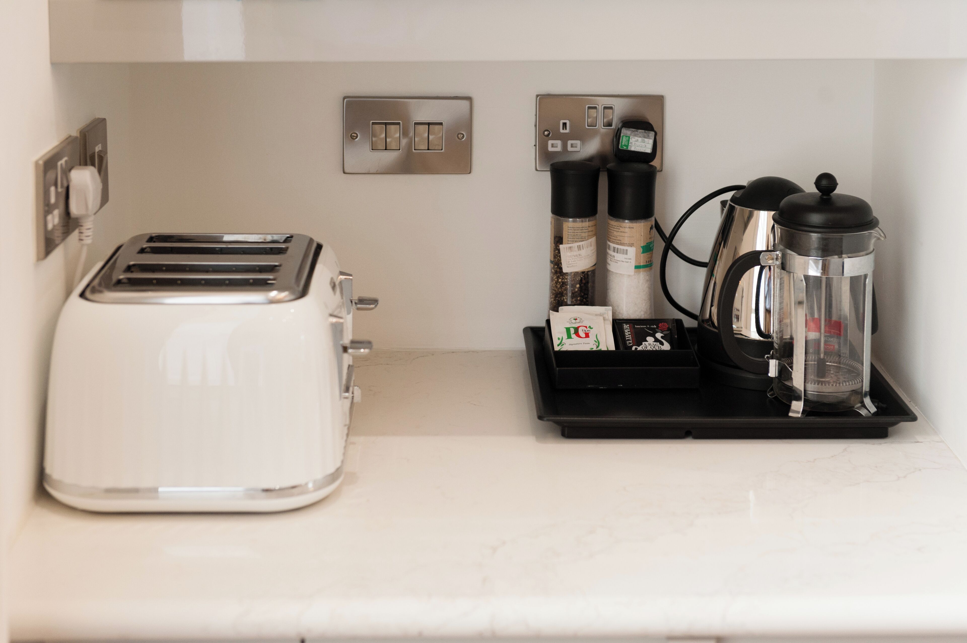 Una kitchenette con una tostadora blanca, una cafetera y una tetera sobre una bandeja negra.