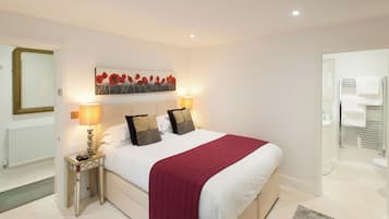 A bedroom with a large bed, two bedside lamps, a red throw blanket, and a painting above the bed.