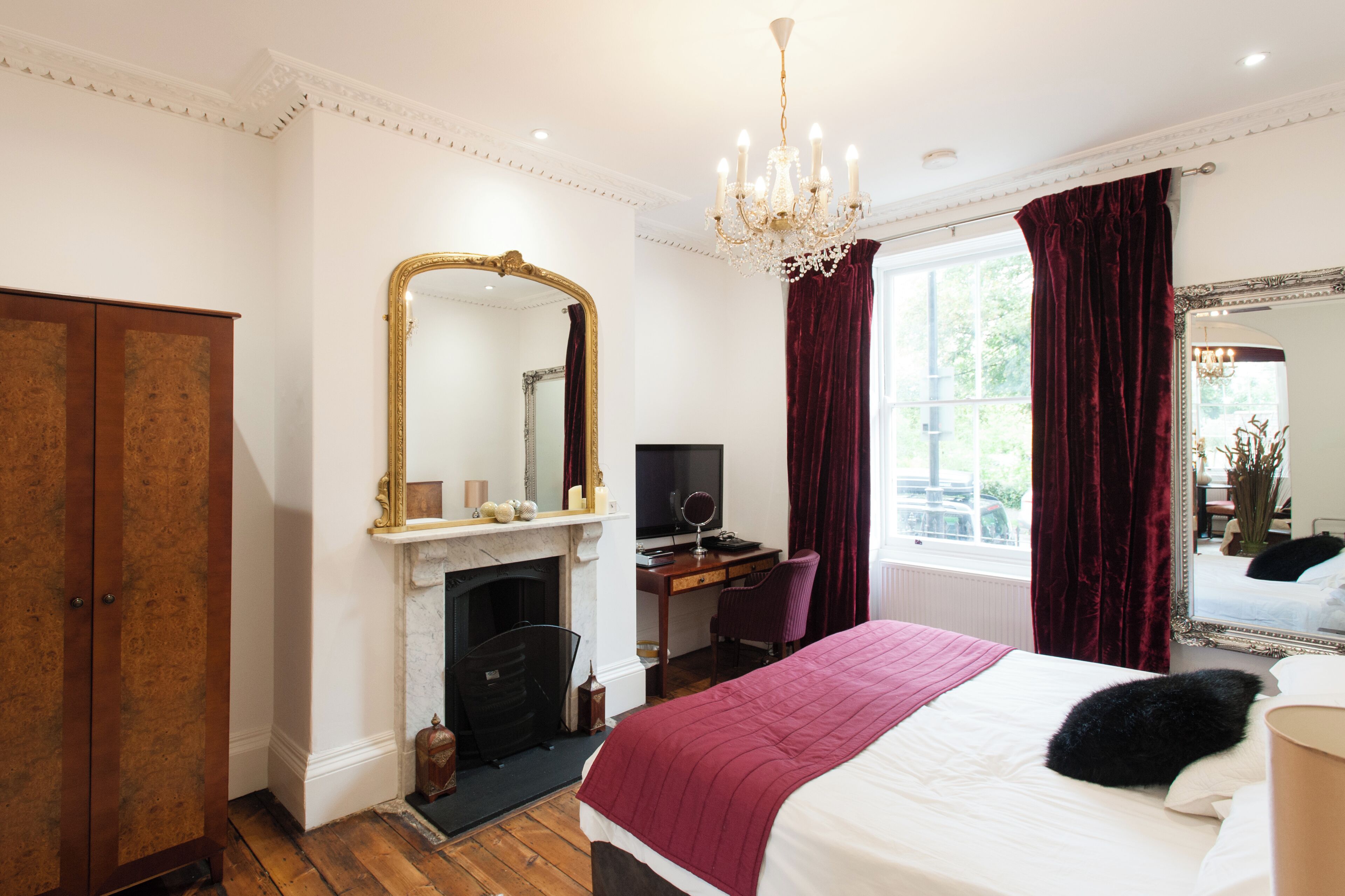 A bedroom with a large bed, a desk with a computer, a fireplace, and a large mirror.