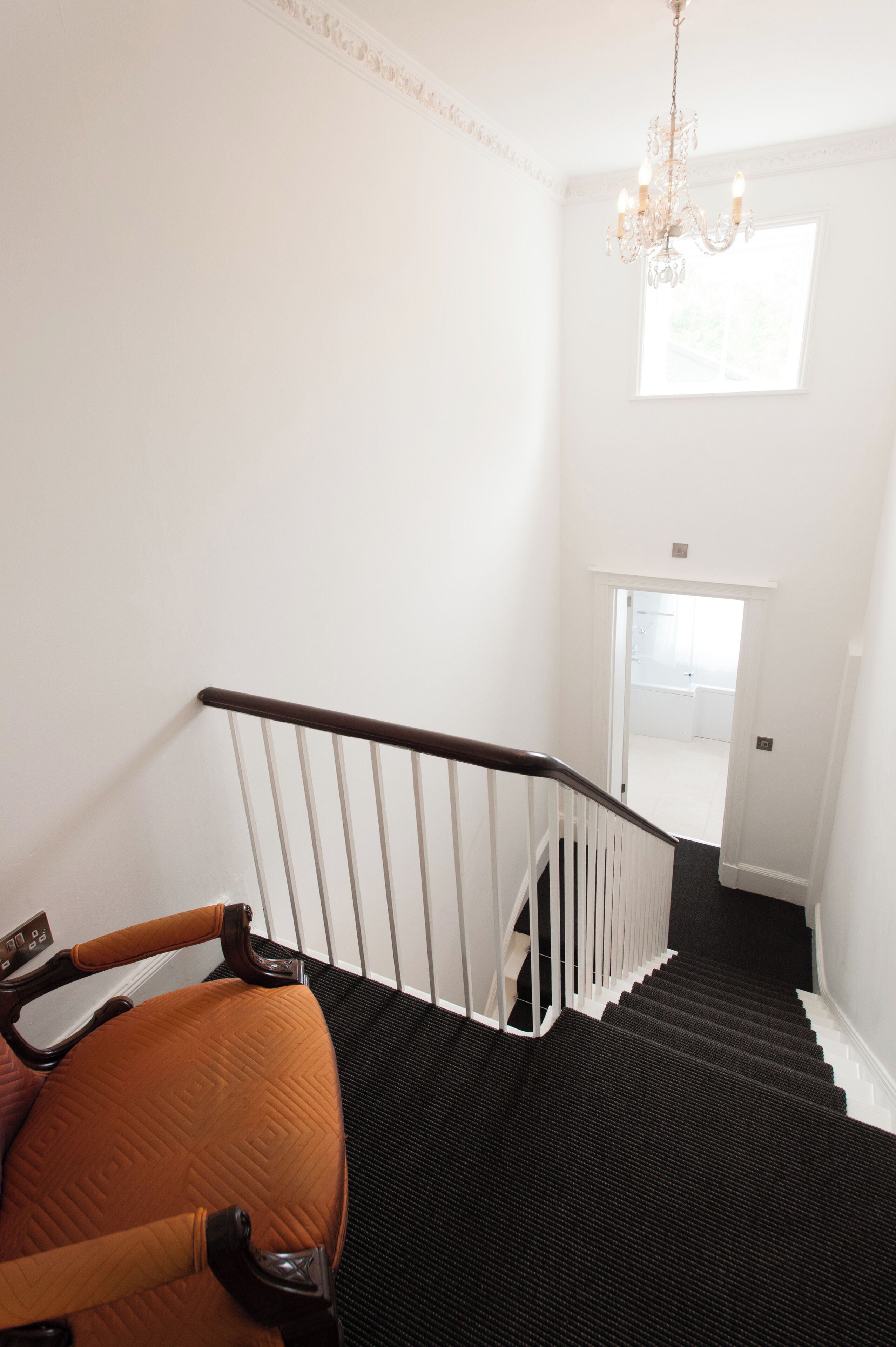 A staircase with a black carpet, white walls, and a chandelier.