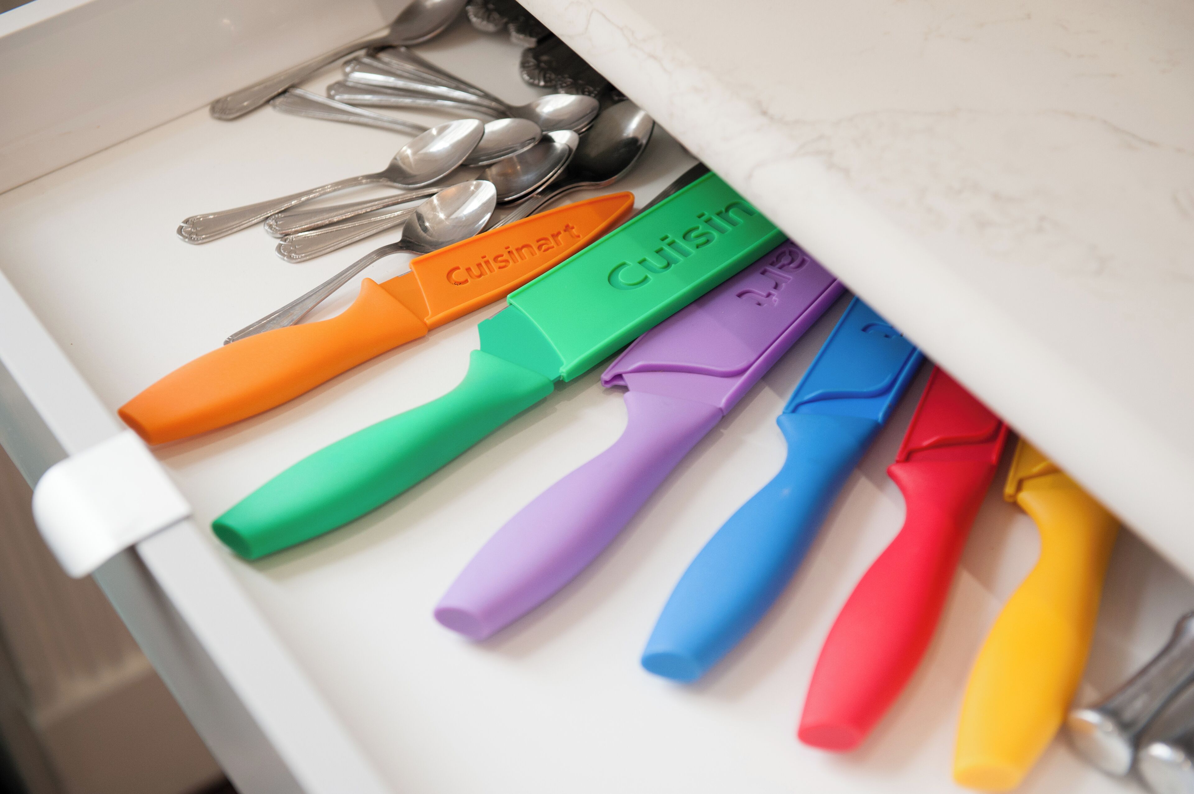 A drawer containing various kitchen utensils and colorful silicone spatulas labeled with brand names.