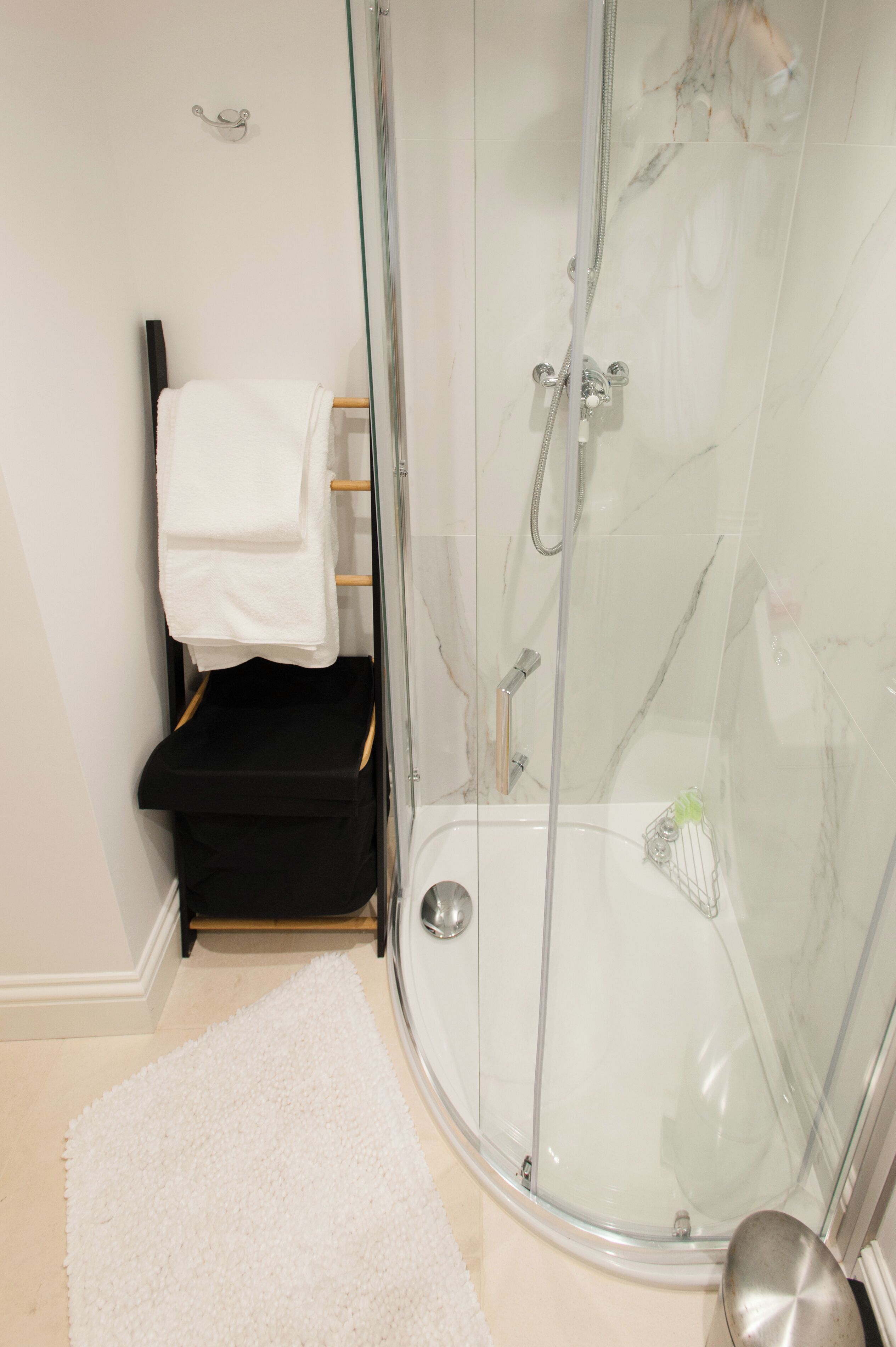 A modern bathroom with a glass-enclosed shower, a white towel on a rack, and a black bench.
