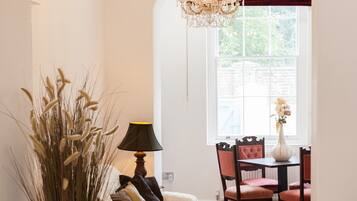 A cozy room with a white sofa, a dining table with chairs, a chandelier, and a window with a view of greenery.