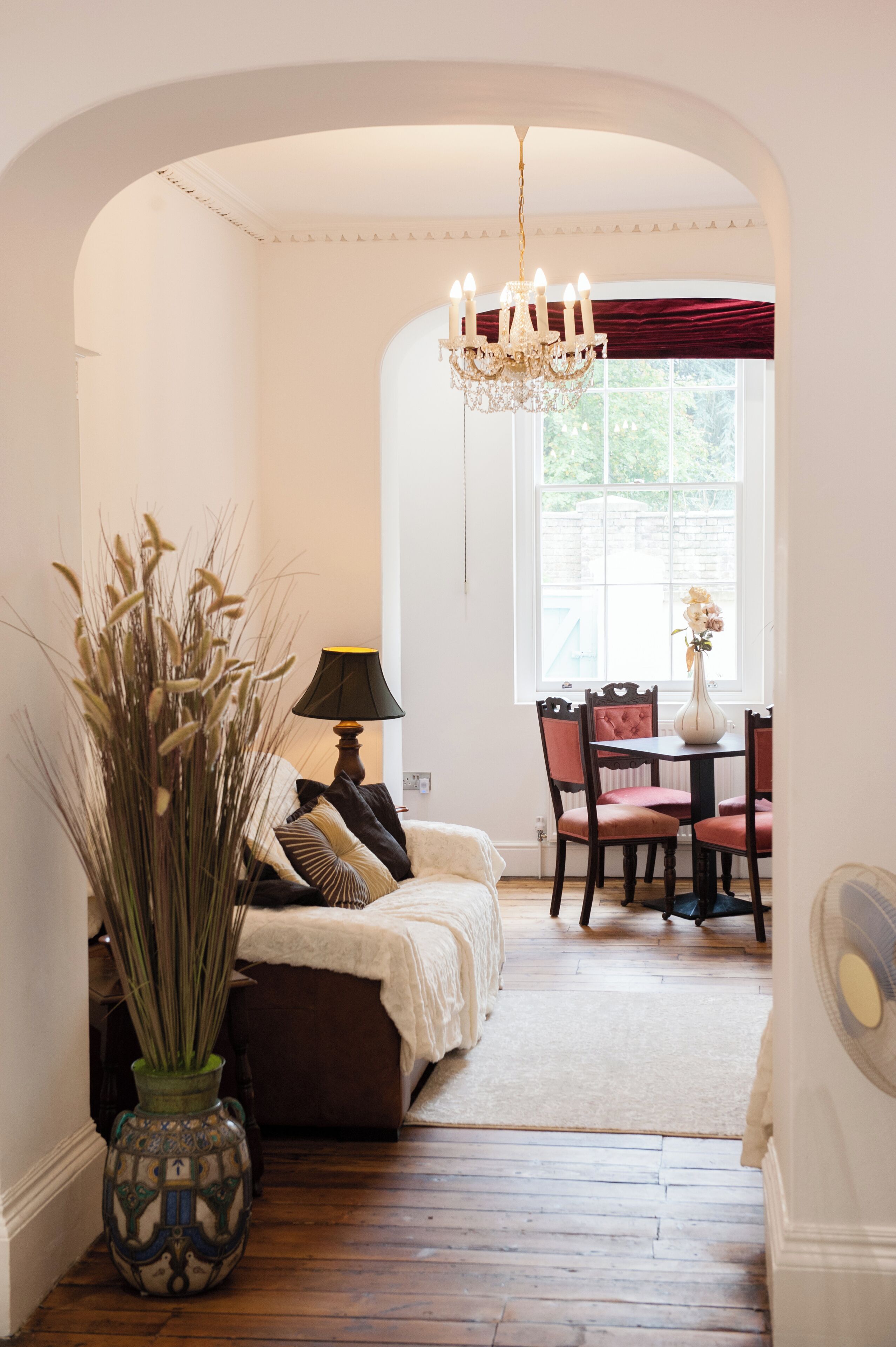 A cozy living room with a sofa, a dining table with chairs, a chandelier, and a vase of flowers.