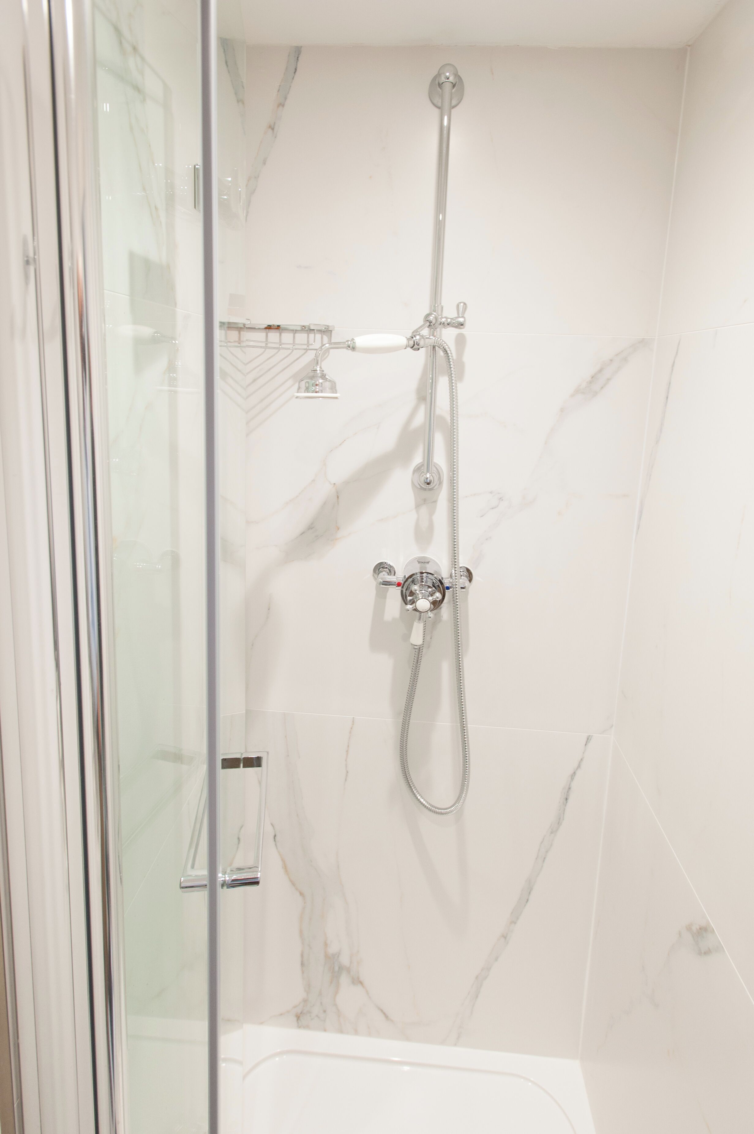 A modern bathroom with a glass-enclosed shower, marble walls, and a white bathtub.