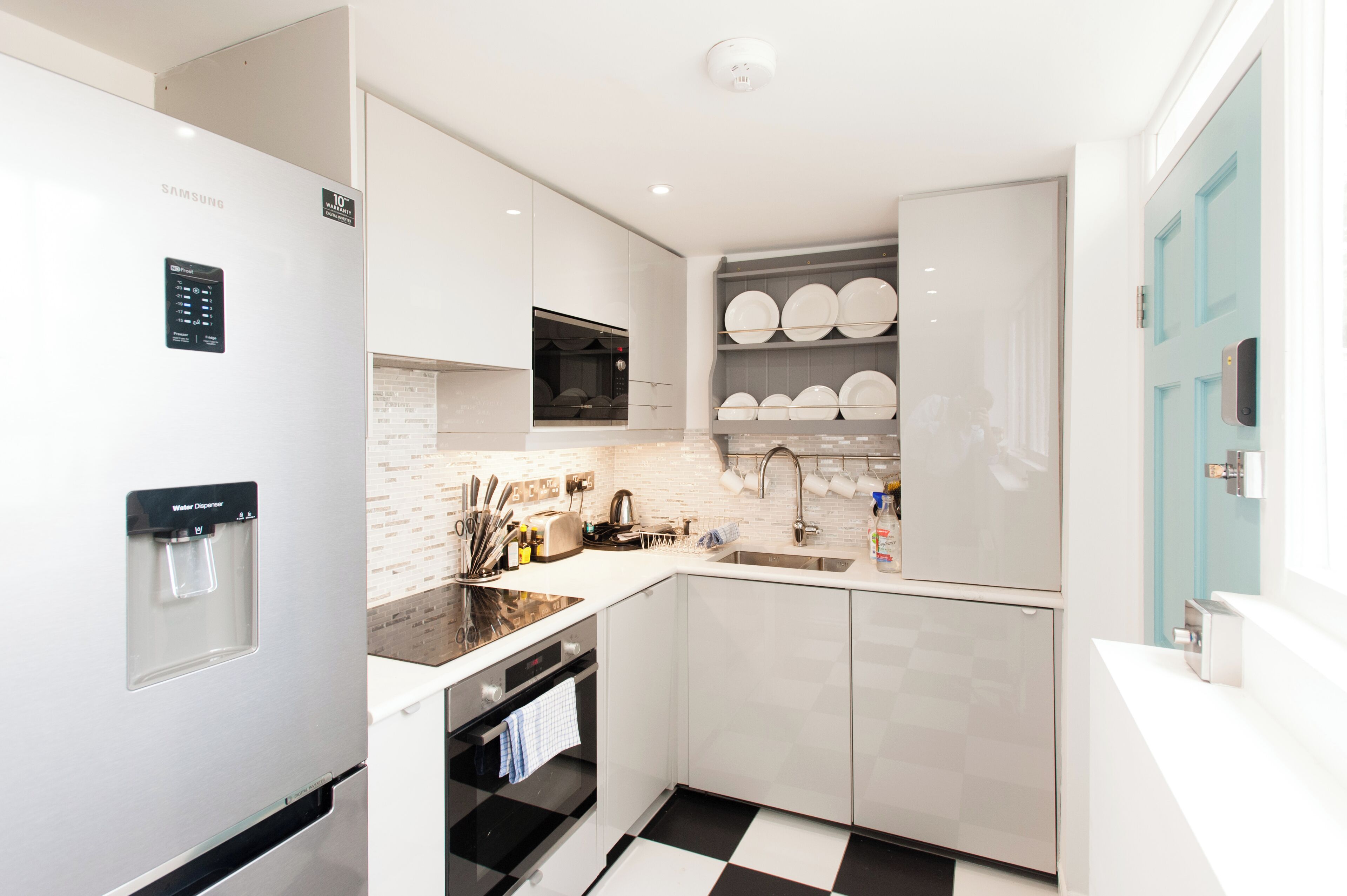 Een moderne keuken met witte kastjes, een ingebouwde oven, een waterdispenser en een spoelbak.