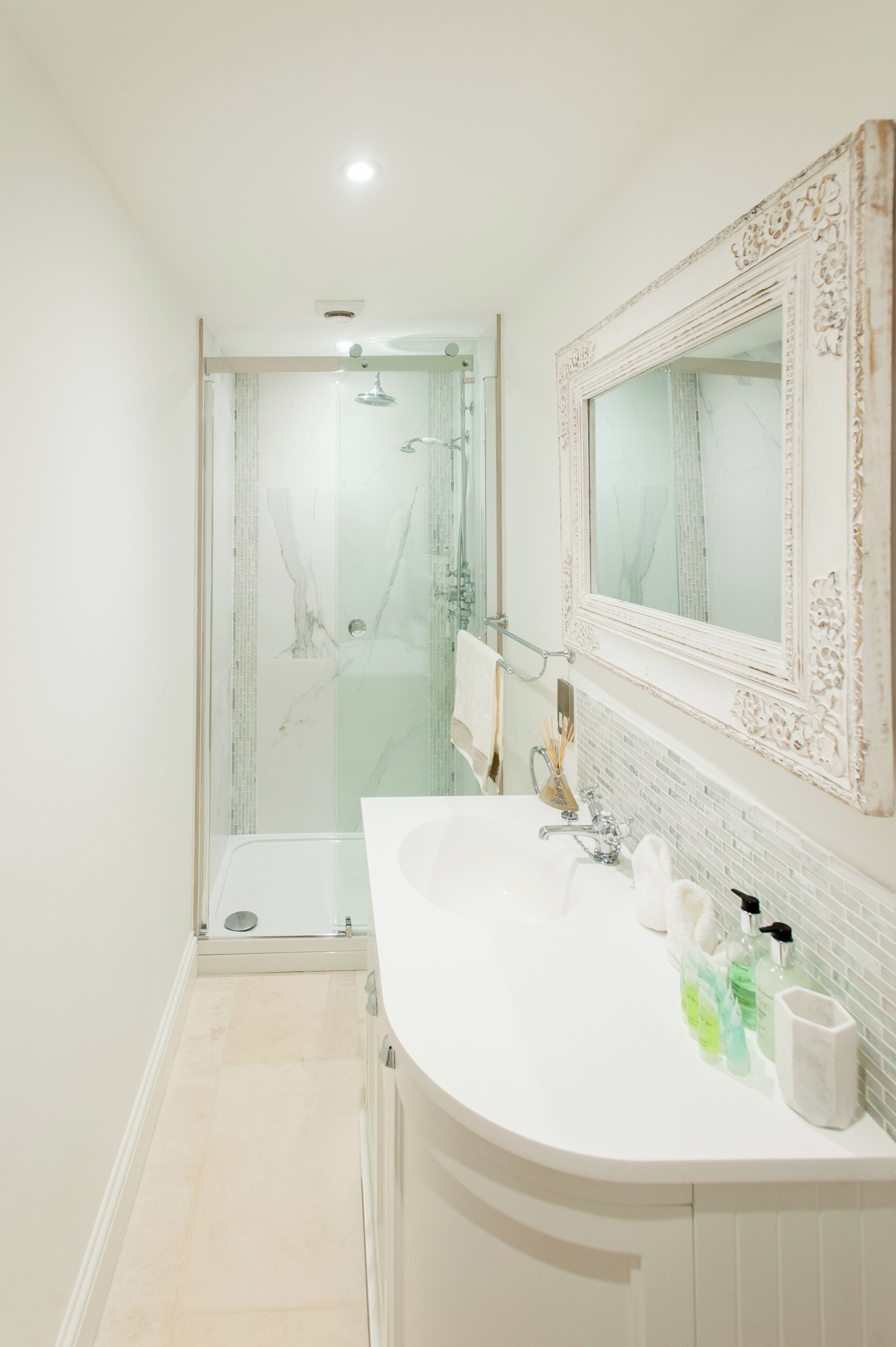 Un bagno moderno con cabina doccia in vetro, un lavandino bianco con uno specchio grande e un pavimento piastrellato.