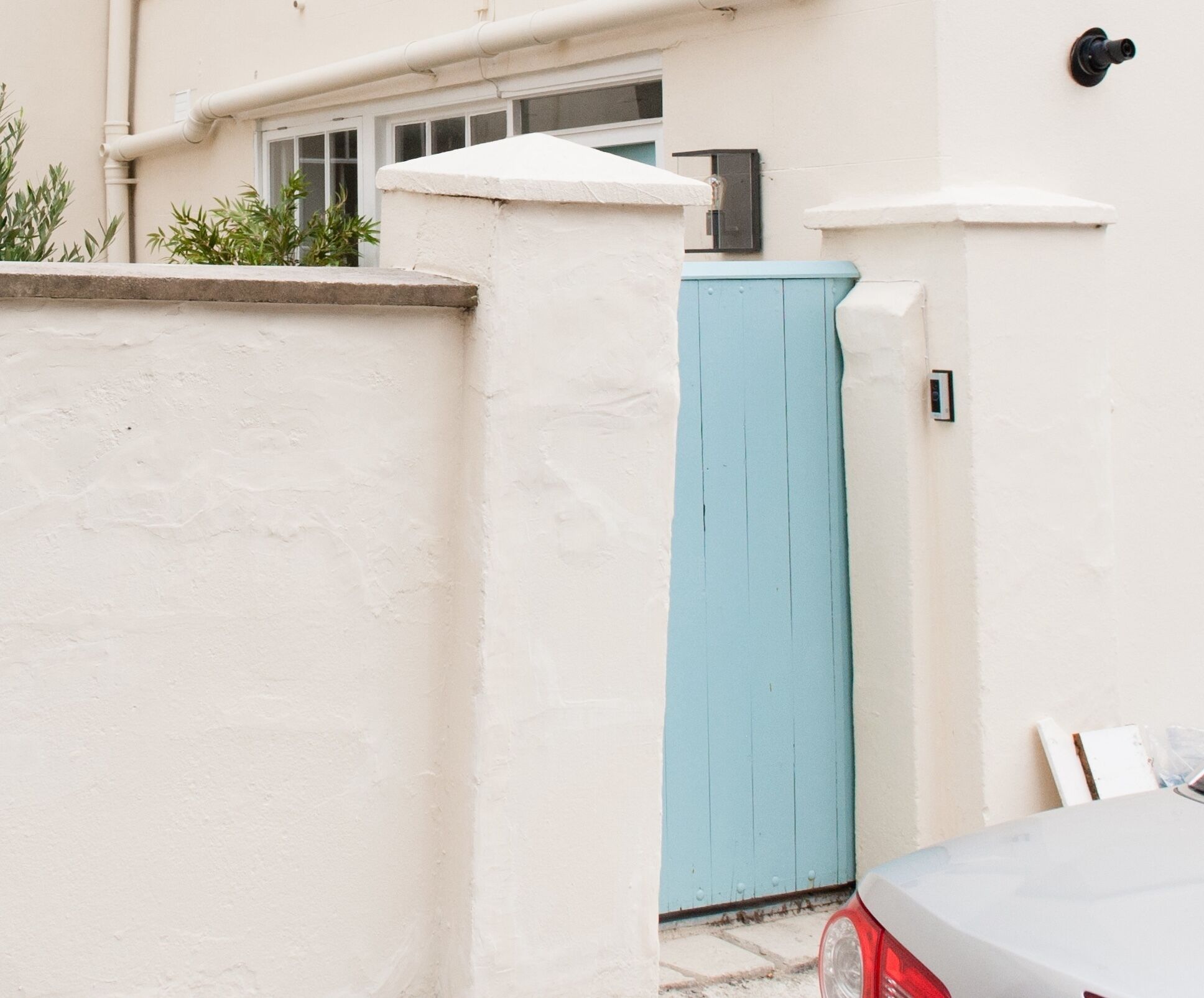 Un edificio blanco con una puerta azul, una ventana y un pequeño espacio exterior con plantas.