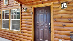 Eine Blockhütte mit Holztür, zwei Fenstern und Außenbeleuchtung.