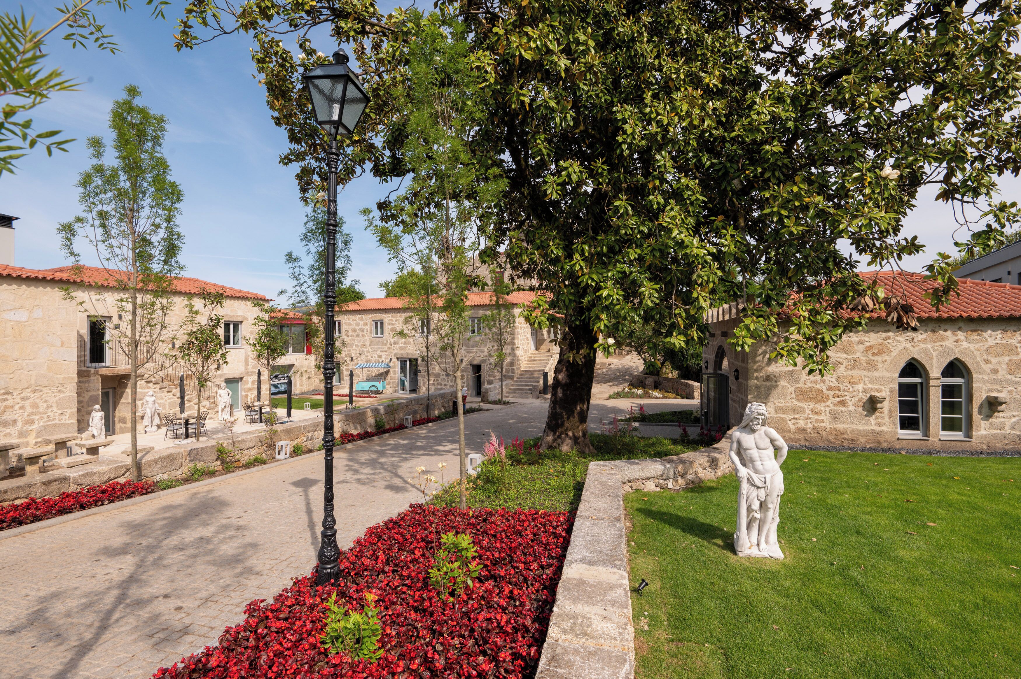 A courtyard with stone buildings, a statue, and red flowers.