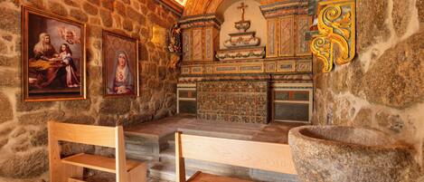 Una capilla de paredes de piedra con bancos de madera, una pila de piedra para bautismos y pinturas religiosas.