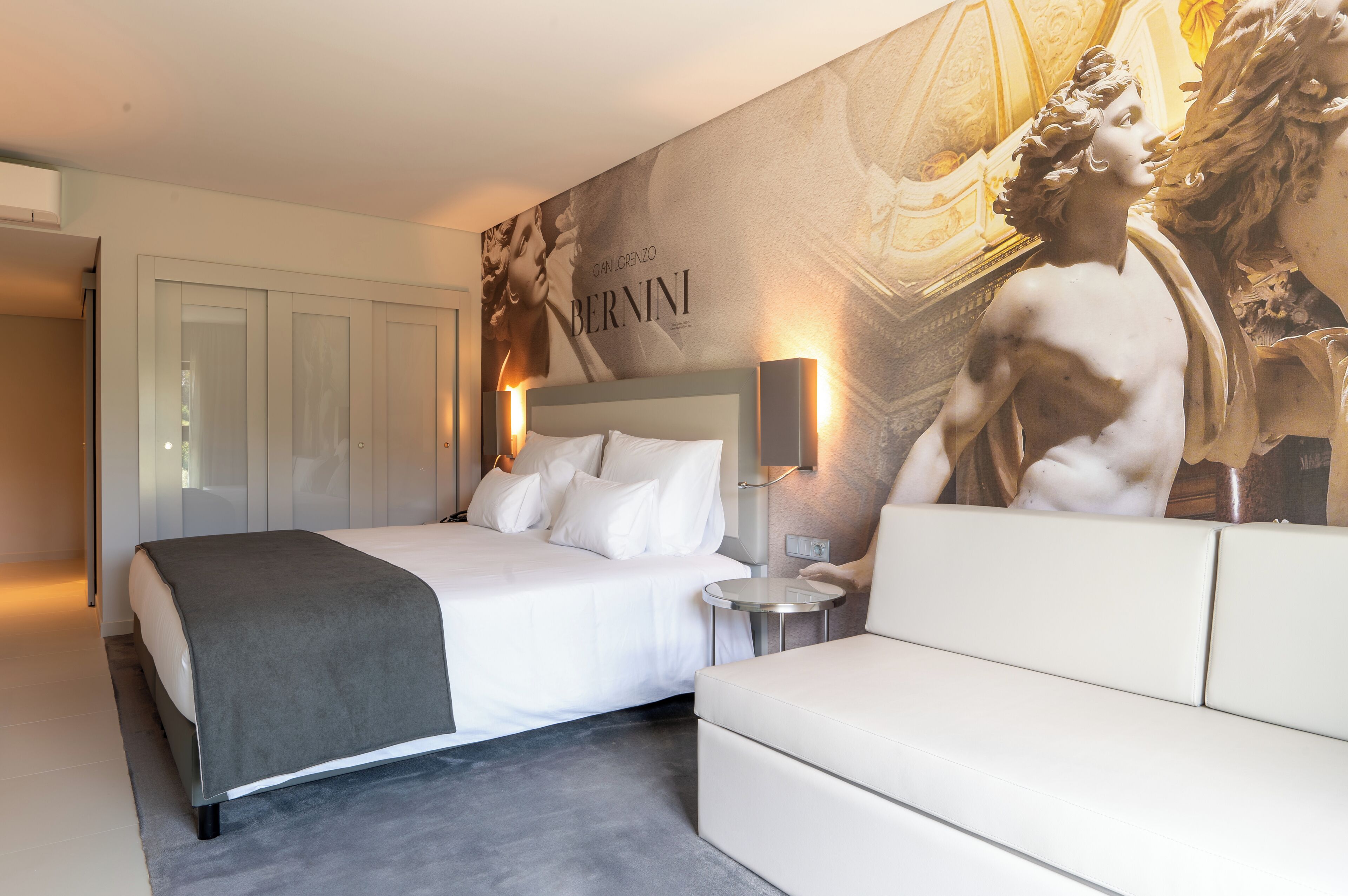 Una habitación de hotel con una cama grande, una mesita de noche, un sofá y una pared decorada con una obra de arte de gran tamaño.