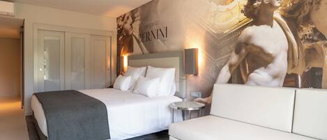 Ein Hotelzimmer mit einem großen Bett, einem Nachttisch, einer Couch und einer Wand mit einem großen Kunstwerk.