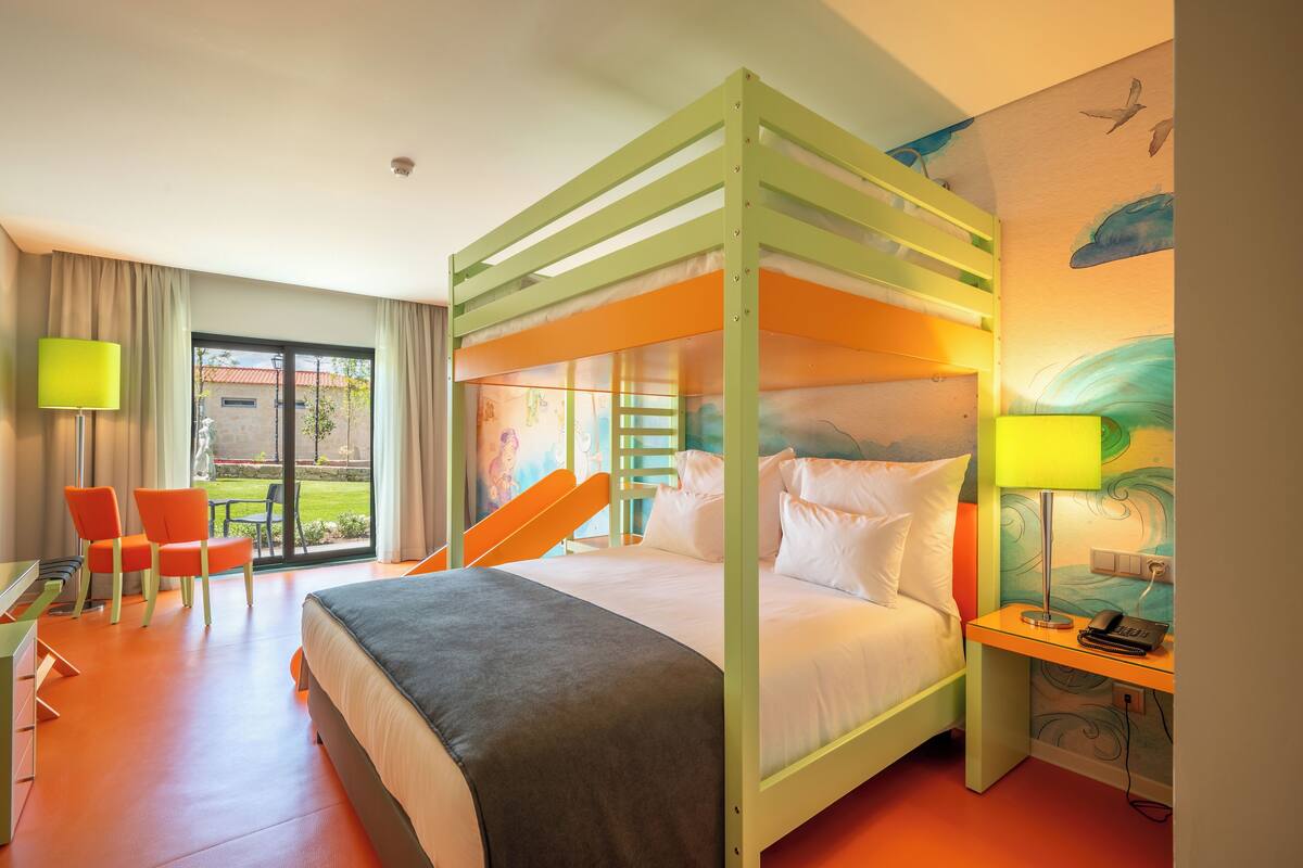 Een kamer met een stapelbed, een bureau met stoel, een lamp en uitzicht op de omgeving.