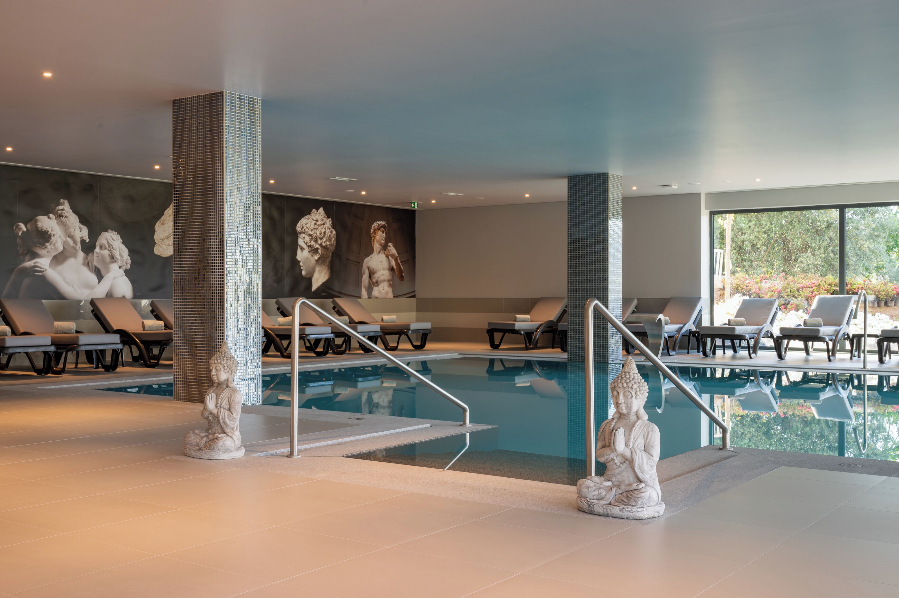A modern indoor swimming pool with lounge chairs and a Buddha statue.