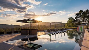 Un área de piscina tranquila con sillones, una pérgola y vistas a colinas distantes.