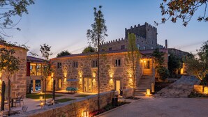 Un edificio de piedra con una torre al estilo de castillo, mesas al aire libre y un camino pavimentado.