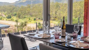 Una mesa de comedor dispuesta con platos, vasos y una botella de vino, con vistas a un paisaje de colinas y viñedos.