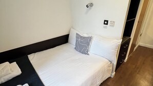 A single bed with white bedding and a black headboard, a black and white patterned pillow, and a folded white towel on the left side. - 6 Bed Apartment @ Astor House by Pureserviced (Plymouth)