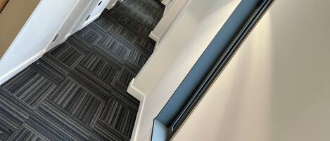 A modern hotel corridor with a patterned carpet, white walls, and a wooden door.