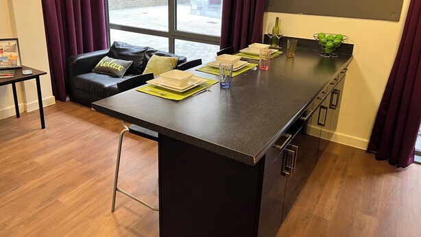 Una cocina moderna con una encimera oscura, un taburete de bar y una zona de comedor con un sofá de cuero negro y una mesita.