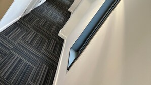 Un interior moderno con una escalera alfombrada, paredes blancas y una puerta de madera.