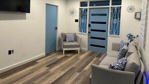 A modern living room with a grey sofa, a grey armchair, and a TV mounted on the wall. - 2-bedroom house in peaceful Lower Carlton w/ AC, WiFi. Within steps of the beach (Lower Carlton)
